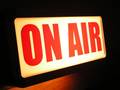 Rote Leuchtbuchstaben "on air" vor dunklem Hintergrund