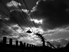 Stacheldrahtzaun mit Lampe und düsteren Wolken in schwarz/weiß. Dieses Bild entstand am 10.11.2006 im ehemaligen Konzentrationslager Auschwitz/Birkenau.
